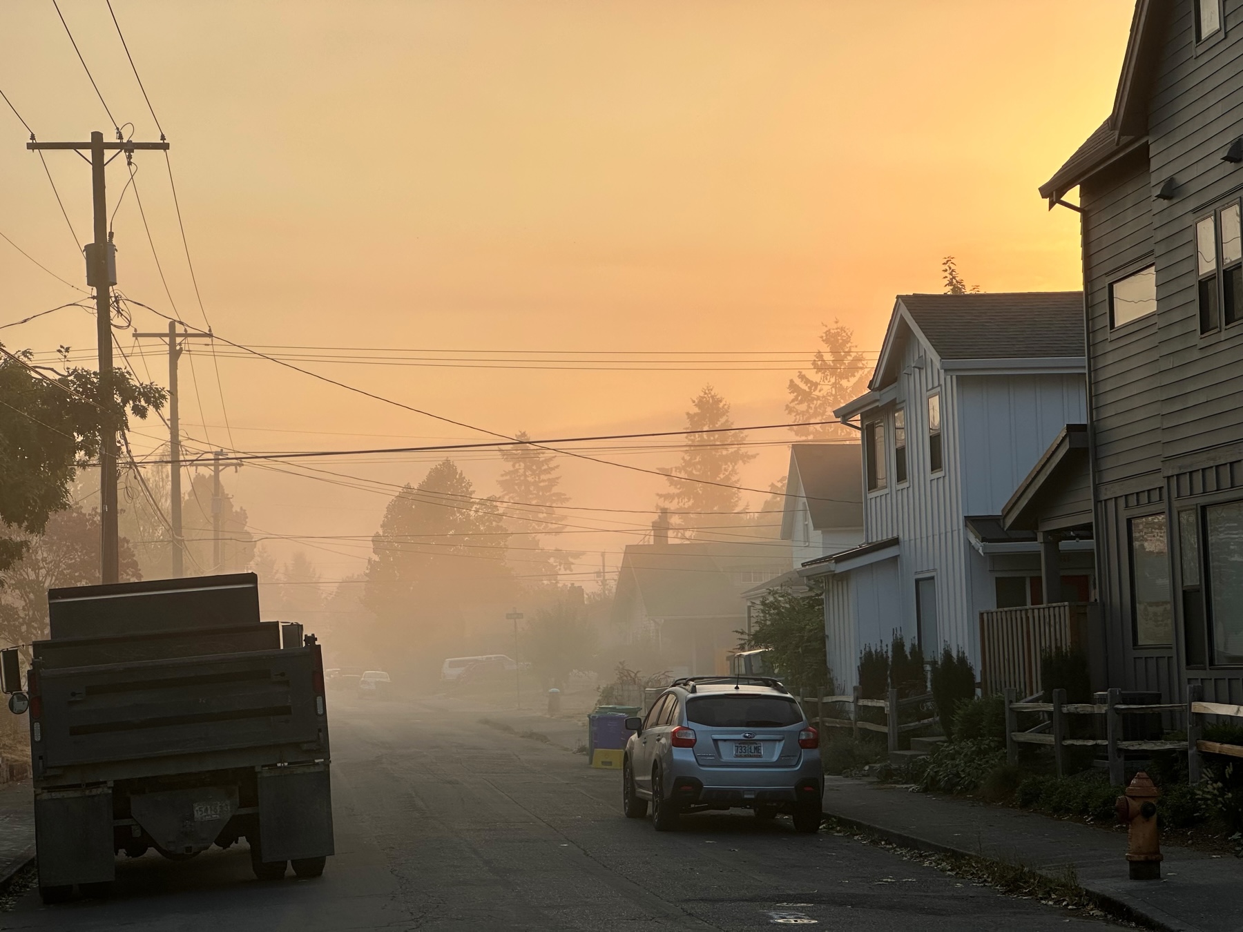 Foggy street view with the sky lit by orange light of the rising Sun.